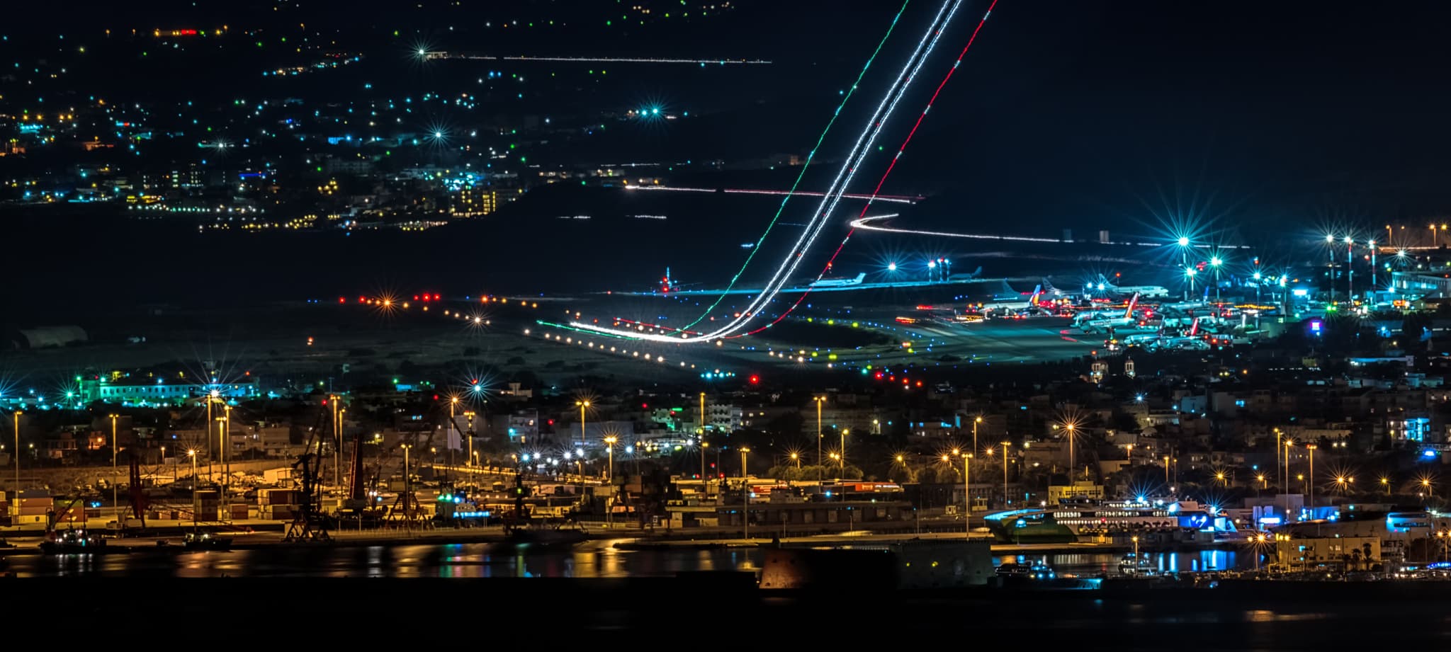 Airport at night with aircraft and vehicle light trails across the apron